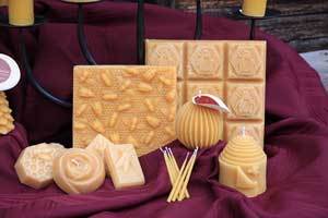 a group of pure beeswax candles and blocks shown on a burgundy linen draped on a table