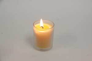 a pure beeswax votive candle burning in a glass votive candle holder