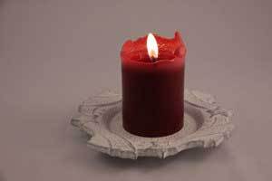 red pure beeswax pillar candle burning on a simple grey candle plate