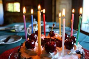 brightly colored beeswax birthday candles lit on a delicious cherry decorated cake