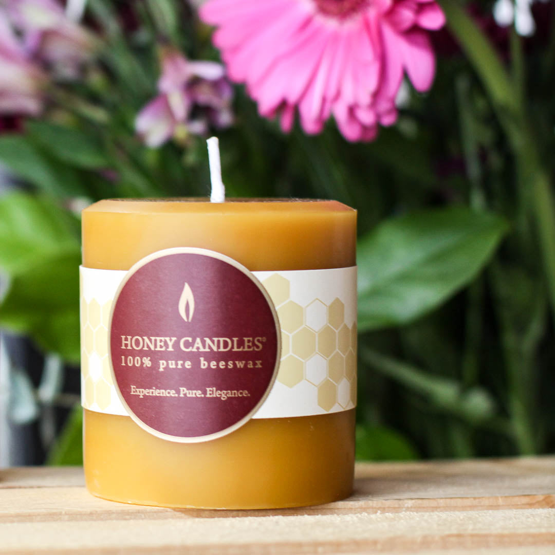 A beeswax pillar candle in a clean kitchen with bright summer flowers