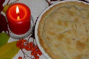 a red pure beeswax candle burning on a table next to a delicious homemade pie