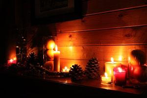 a shelf lightly lit with a grouping of pure beeswax pillar candles and tealight candles next to pine cones for decoration
