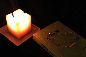 beeswax tealight candle in a holder next to a novel and a pair of reading glasses