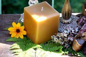 pure beeswax square pillar candle on greenery next to decorative candle holders and flowers