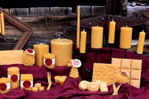 a wide shot of a grouping of natural color beeswax candles in many different size and shapes on a burgundy cloth 
