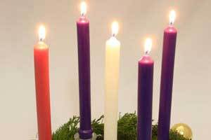 beautiful beeswax purple, white and pink advent candles burning in the center of a evergreen Christmas wreath