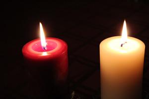 a red and a white pure beeswax column candles burning side by side with a black background