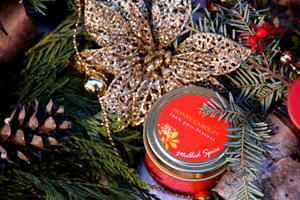 pure beeswax essential tin candle nestled in greenery with gold poinsettia holiday decorations