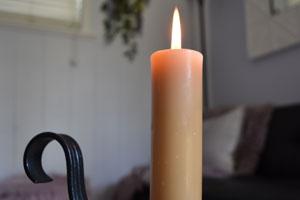 Honey Candles' pure beeswax column candle burning on a black iron candle holder laid on a coffee table with a chair in the background