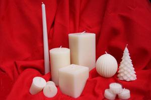 a grouping of white pure beeswax candles in various shapes and styles on a red blanket