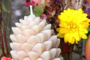 a unique pine cone beeswax candle nestled in a fall arrangement with berries and apples and yellow flowers