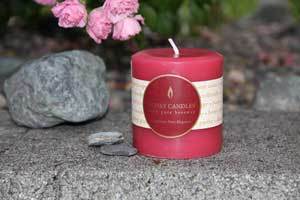 Pretty pink three inch beeswax pillar candle on a grey stone wall  and grey rocks nearby