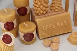 a block of natural pure beeswax with pillar, sphere, tea light, pine cone candles set around it all showing the burgundy Honey Candles logo