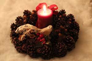red beeswax candle nestled in the center of a homemade Christmas wreath that has a bird decoration on them