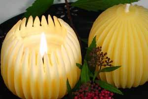 two beeswax fluted sphere candles side by side, one is lit the other isn't 