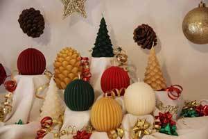 Christmas display showcasing pure beeswax candles in tree, pine cone and sphere shapes and Christmas colors of red, green, white and natural