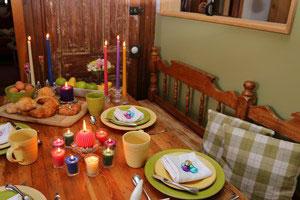 a lovely country oak dining table set with food and plates with a grouping of brightly colored beeswax candles in a circle in the center of the table