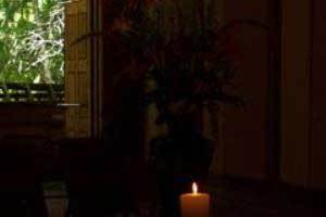 a simple beeswax candle burning in a very dark room with a small window letting in a little bit of light