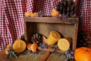 pure beeswax votive candles in a box with oranges and pine cone in front of a picnic patterned cloth