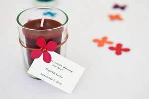 red beeswax votive candle in glass cup with a tag attached used as a wedding favor