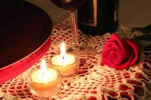 two pure beeswax tealight candles burning on a white lace table cloth next to a red rose perfect for valentines day