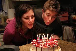 beeswax birthday candles on a lovely birthday cake being blown out by two people 